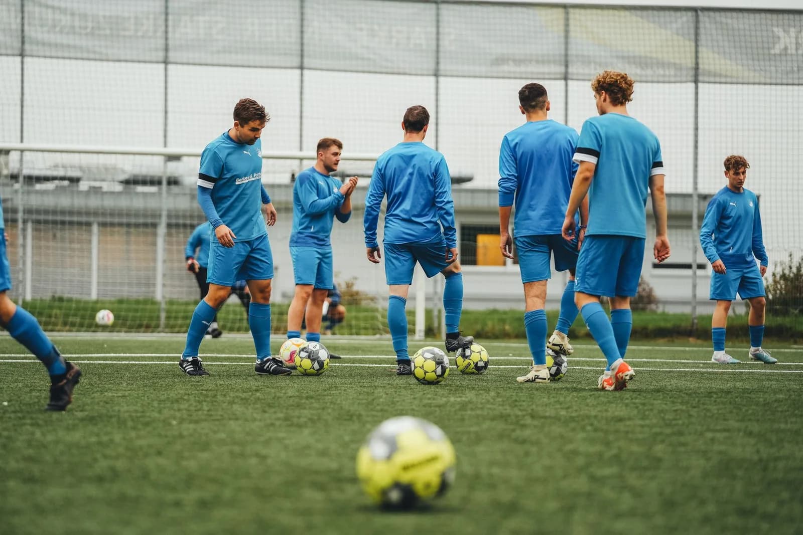 Equip de futbol entrenant amb equipacions esportives blaves, pantalons curts i mitgetes a joc
