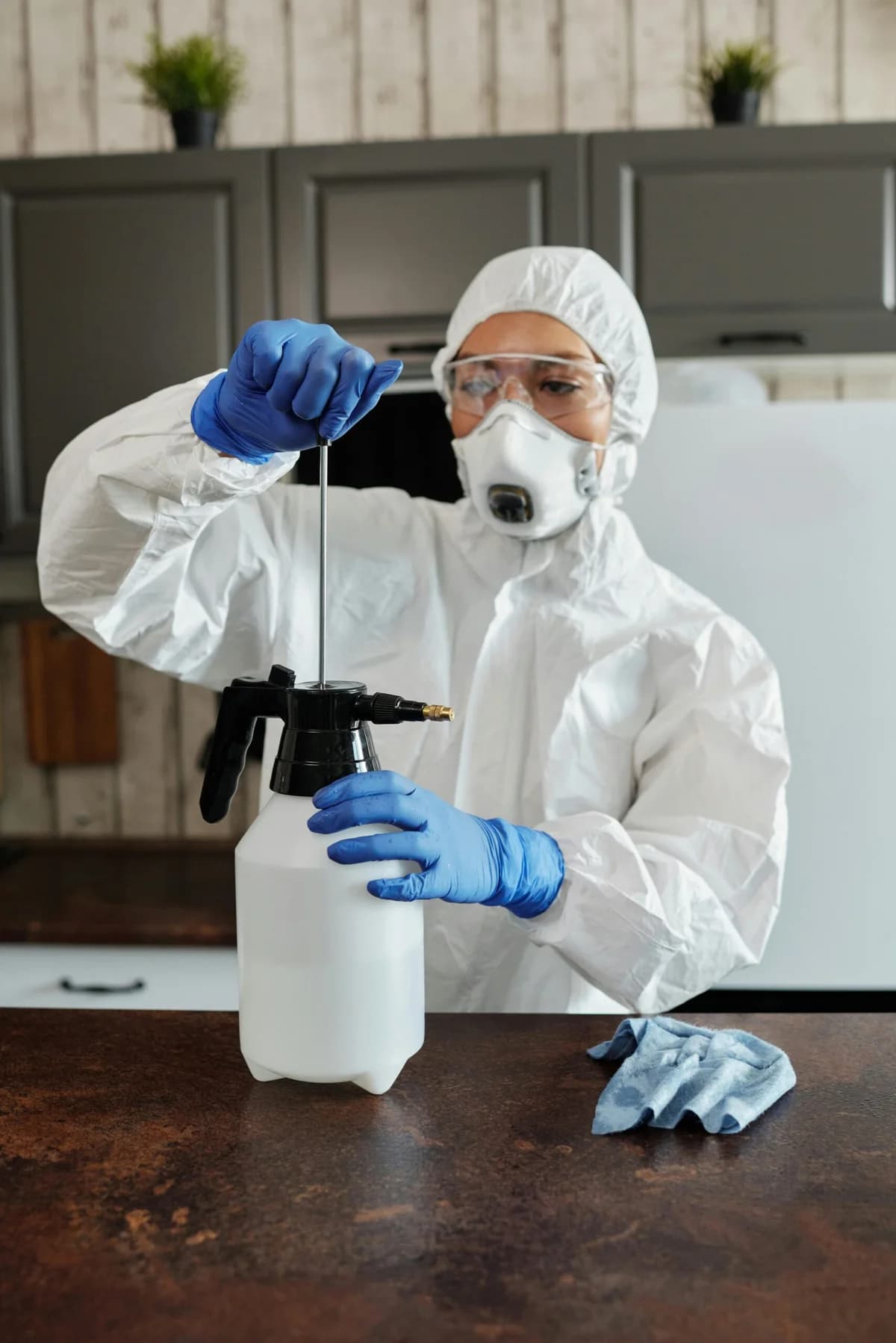 Persona amb guants blaus, ulleres i granota blanca preparant un polvoritzador manual